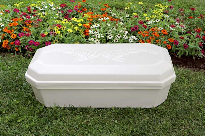 Pet casket in ivory color sitting on grassy lawn with flowers in the background.